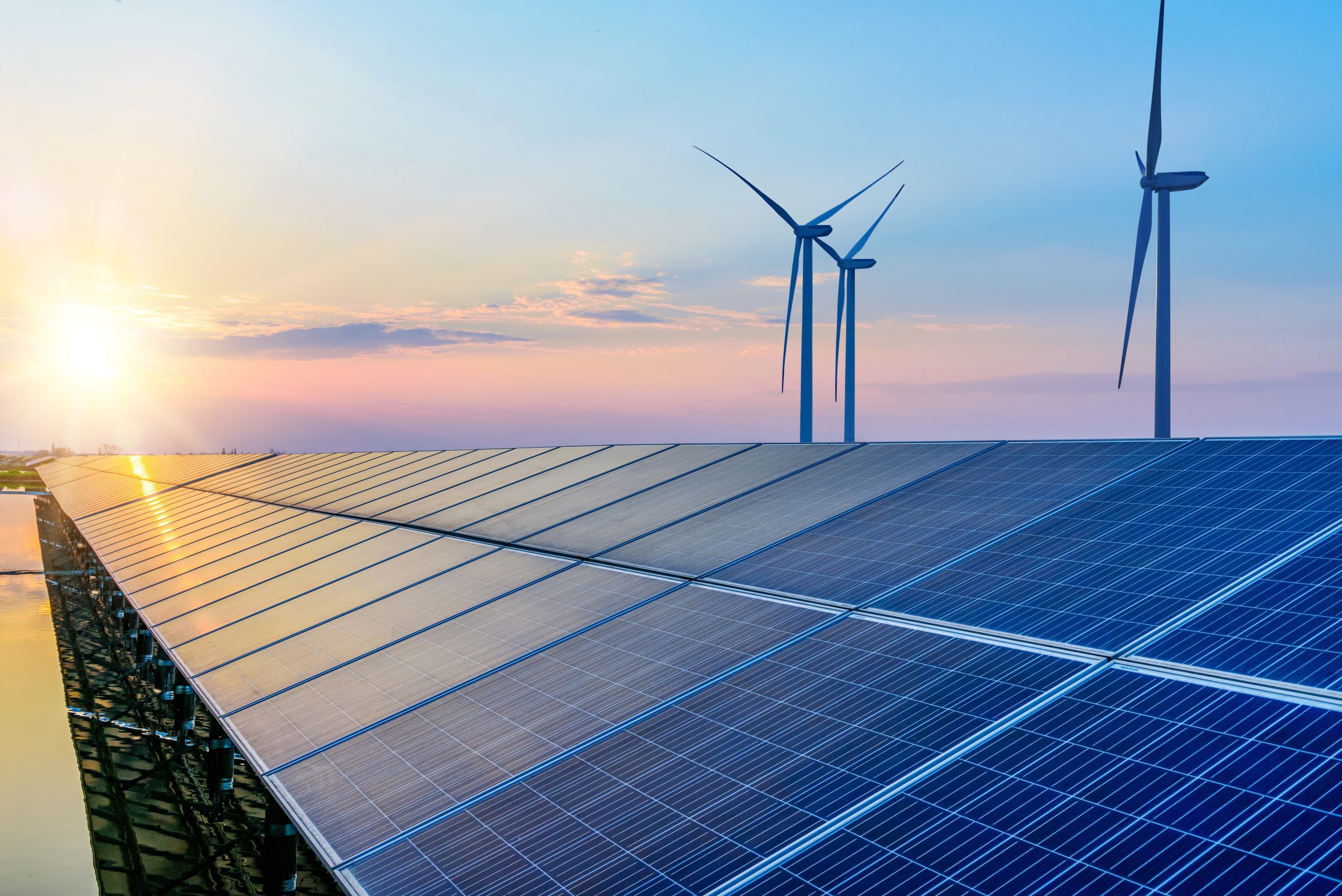 Solar panels and wind turbines in front of a sunset.
