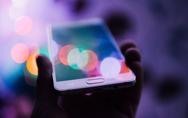 Hand holding a phone with a purple background and multicolour reflection