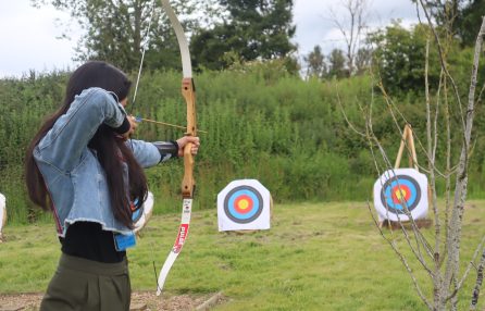 A woman aiming a bow and arrow at a target.