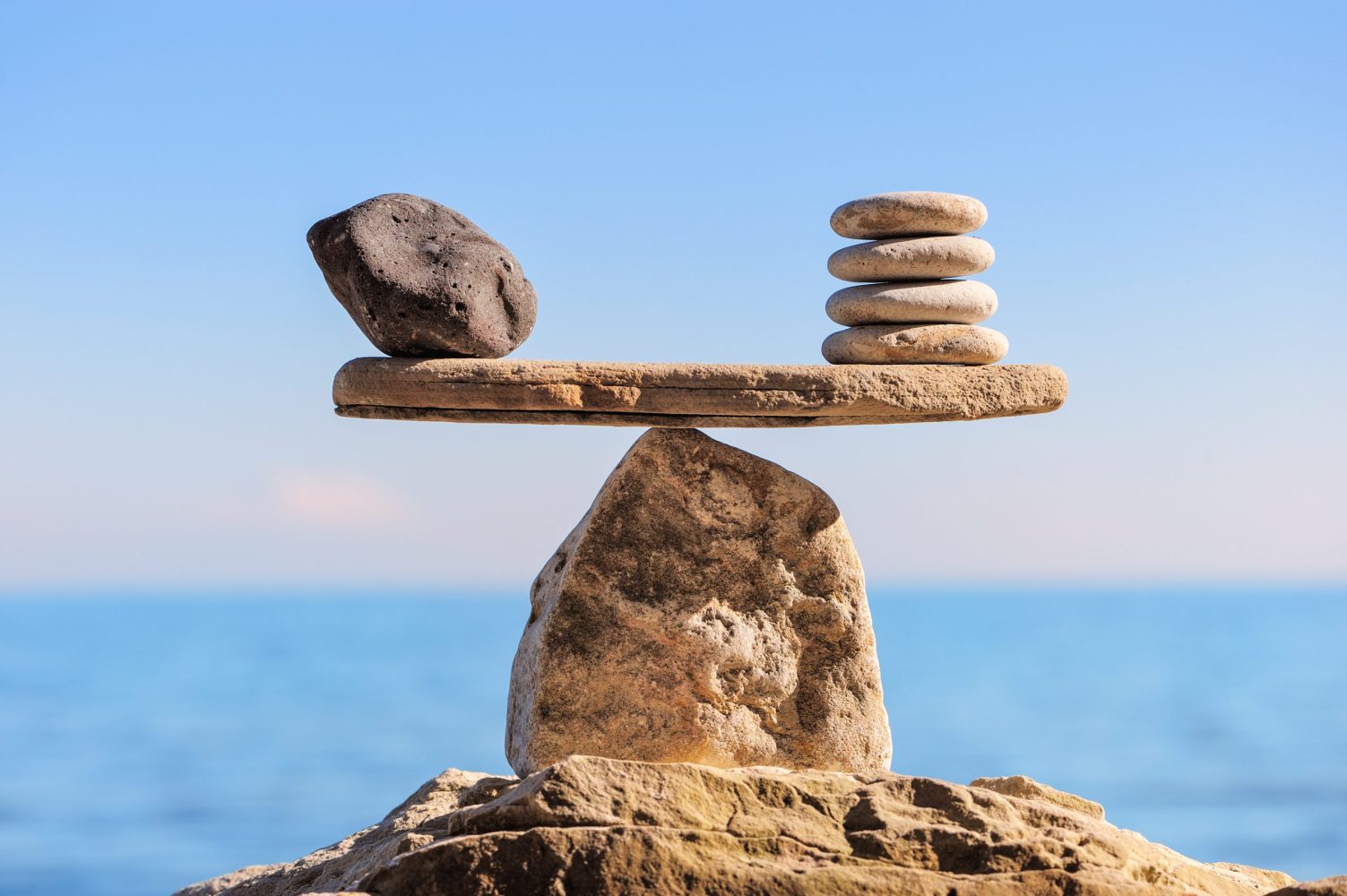 A scale made of rocks showing complete balance in front of calm waves.